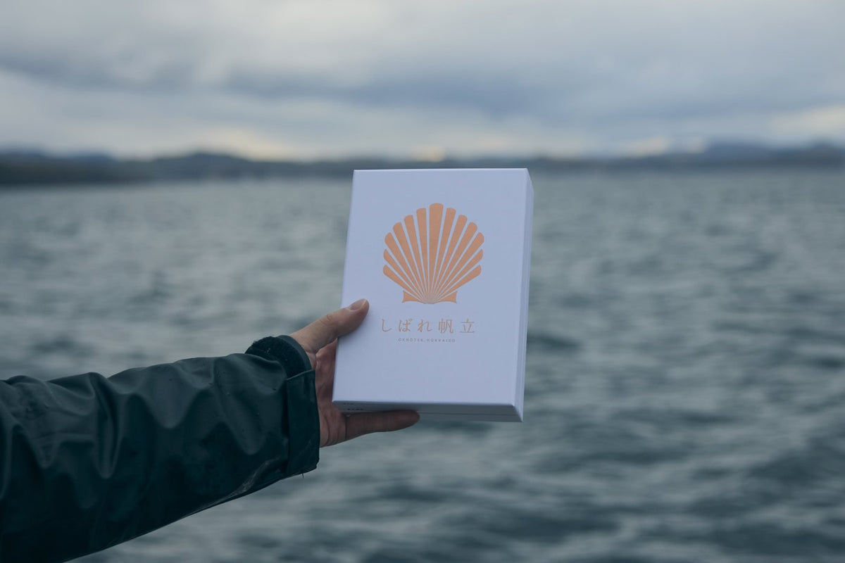 海を背にしばれ帆立の化粧箱を持つ手